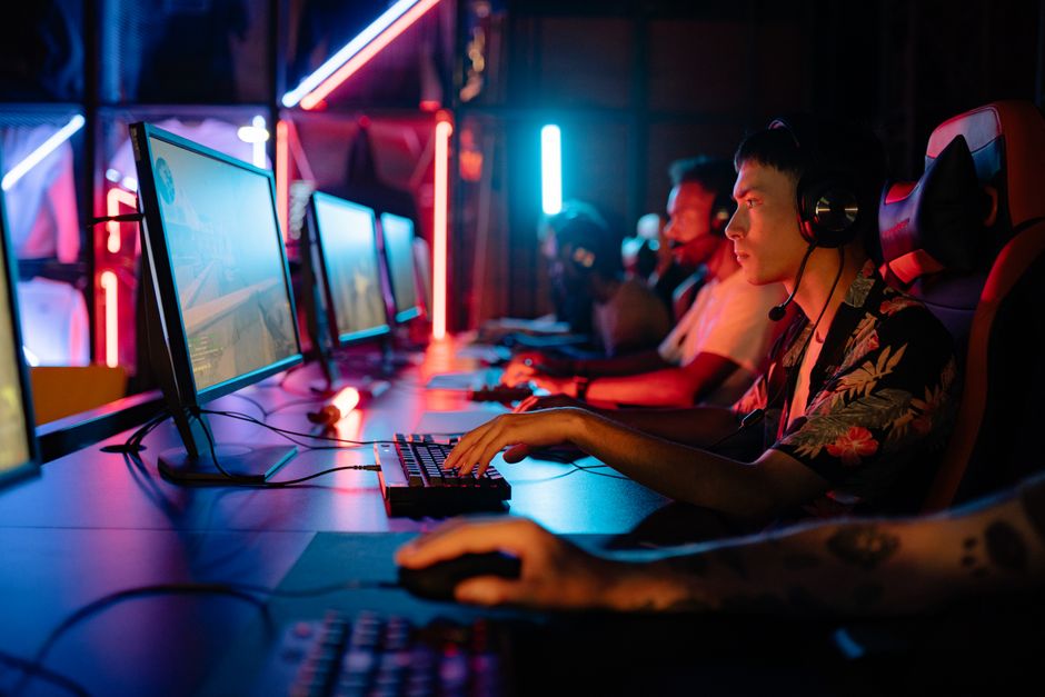 Jovens jogando videogame em um ambiente de gamer com iluminação neon colorida, criando uma atmosfera de diversão e competição.