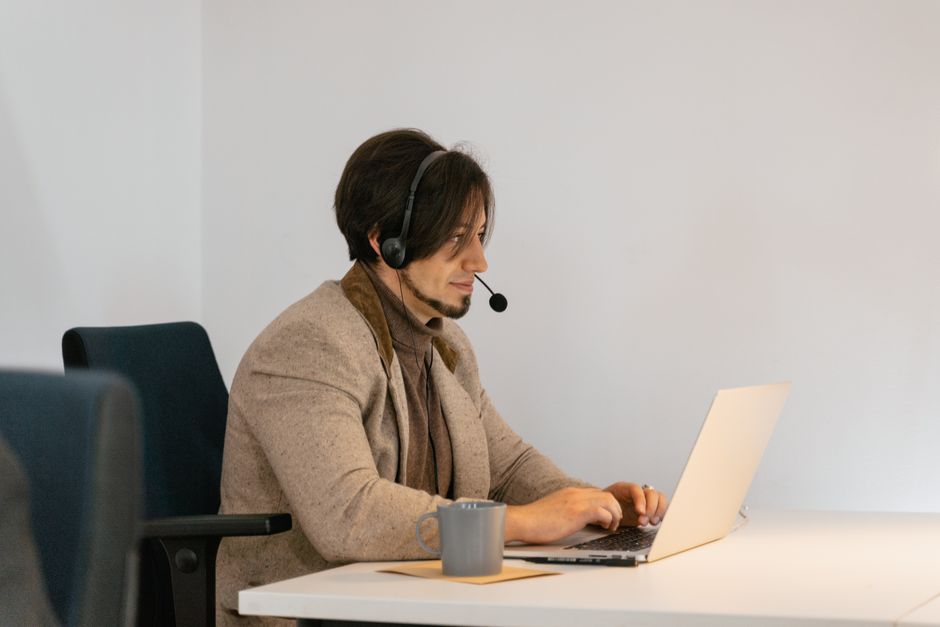 Profissional de suporte ao cliente usando headset e laptop em ambiente de trabalho para atendimento remoto.
