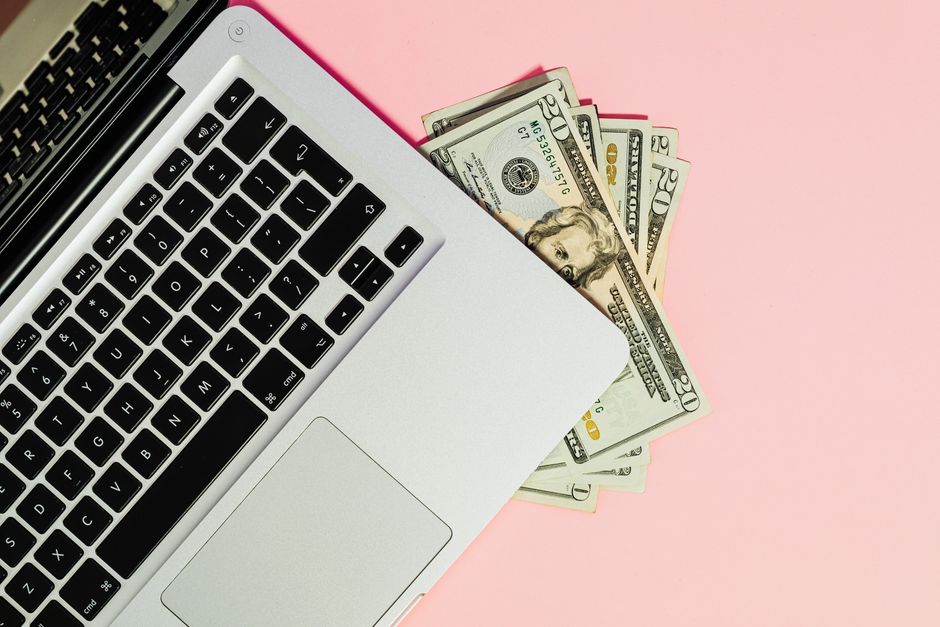 Imagem de um laptop com dinheiro em notas de dólar ao lado, simbolizando gestão financeira e recursos digitais.
