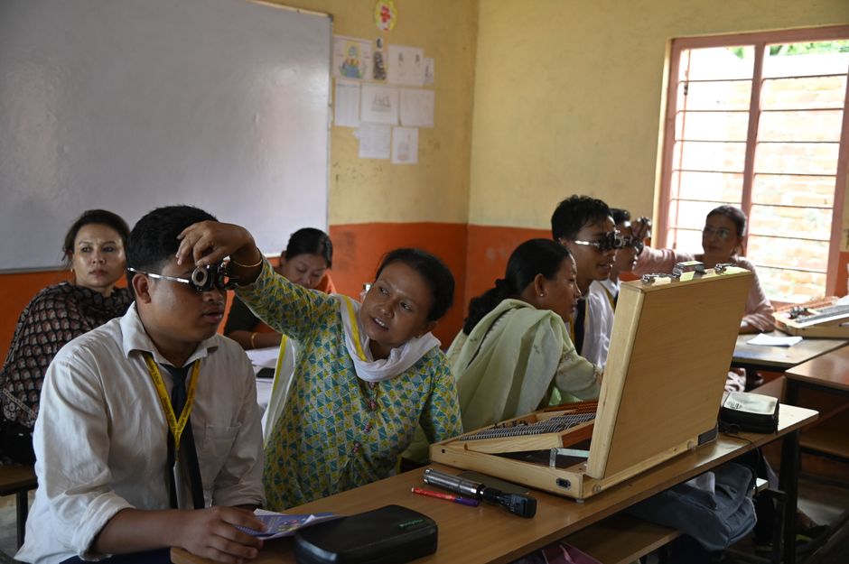Professora realizando exame de vista em sala de aula com estudantes, promovendo atividades de saúde ocular na escola.