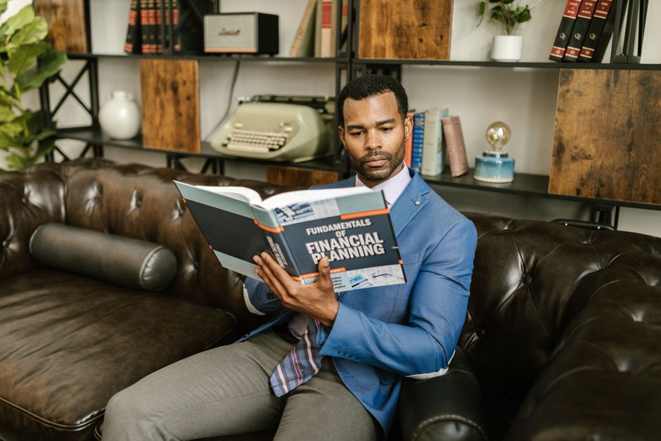 Homem lendo um livro sobre planejamento financeiro em um ambiente de escritório moderno.