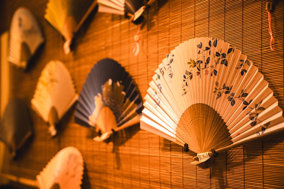 Imagem de leques decorativos com design floral, exibidos na parede de um ambiente ao estilo oriental ou inspirado em cultura asiática.
