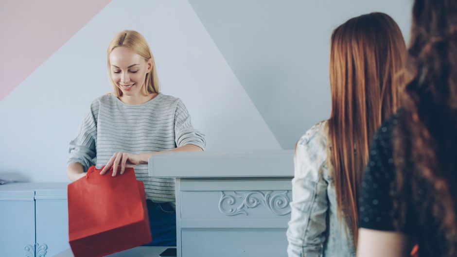 Mulher sorridente entregando presente para clientes ou colegas em ambiente de escritório, simbolizando boas-vindas ou celebração profissional.