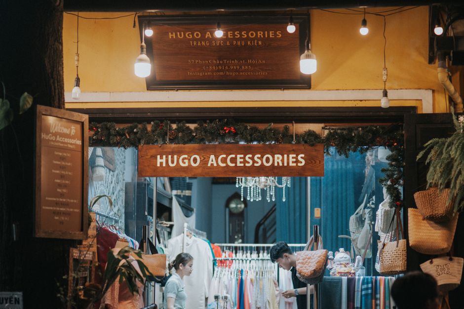 Fachada de uma loja de acessórios com decoração natalina, luzes penduradas e clientes explorando os produtos.