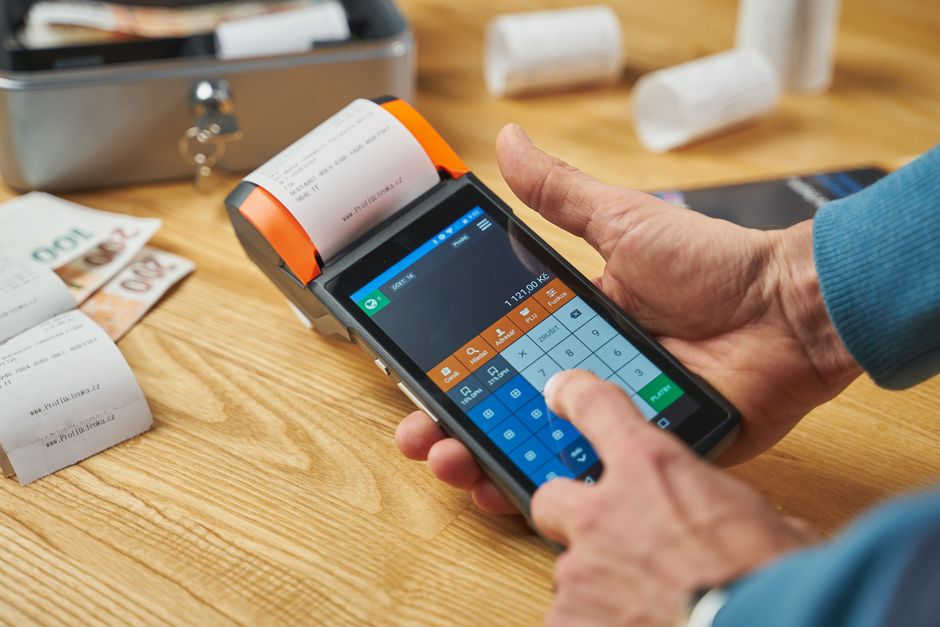 Pessoa realizando uma operação de pagamento utilizando um dispositivo eletrônico de ponto de venda (POS), exemplificando tecnologia e gestão financeira no comércio.