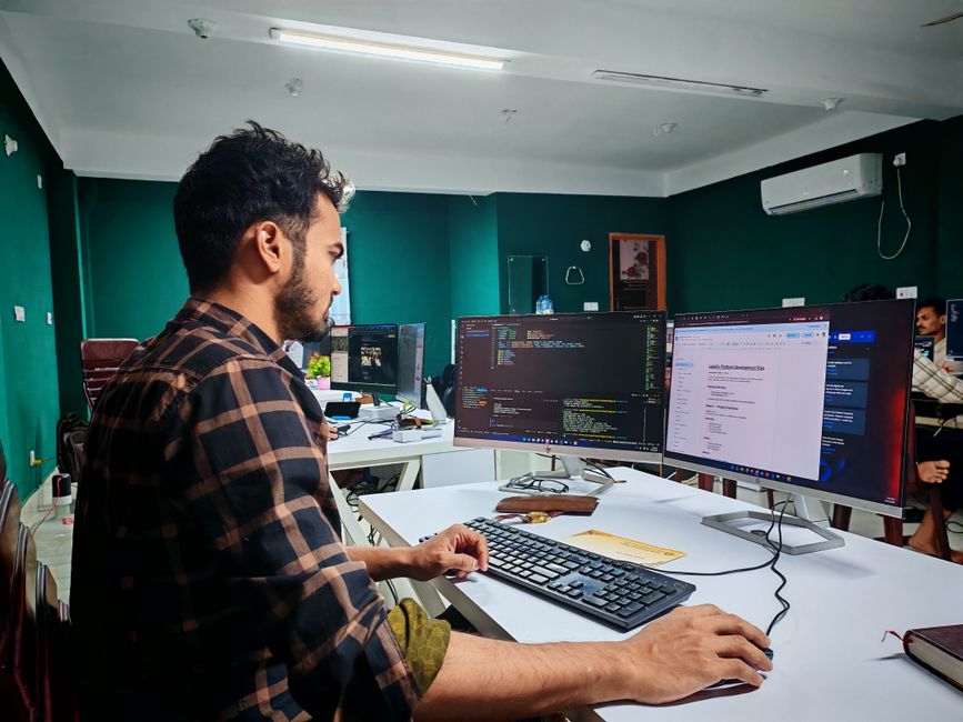 Desenvolvedor de software trabalhando em ambiente de escritório com múltiplos monitores e código aberto.