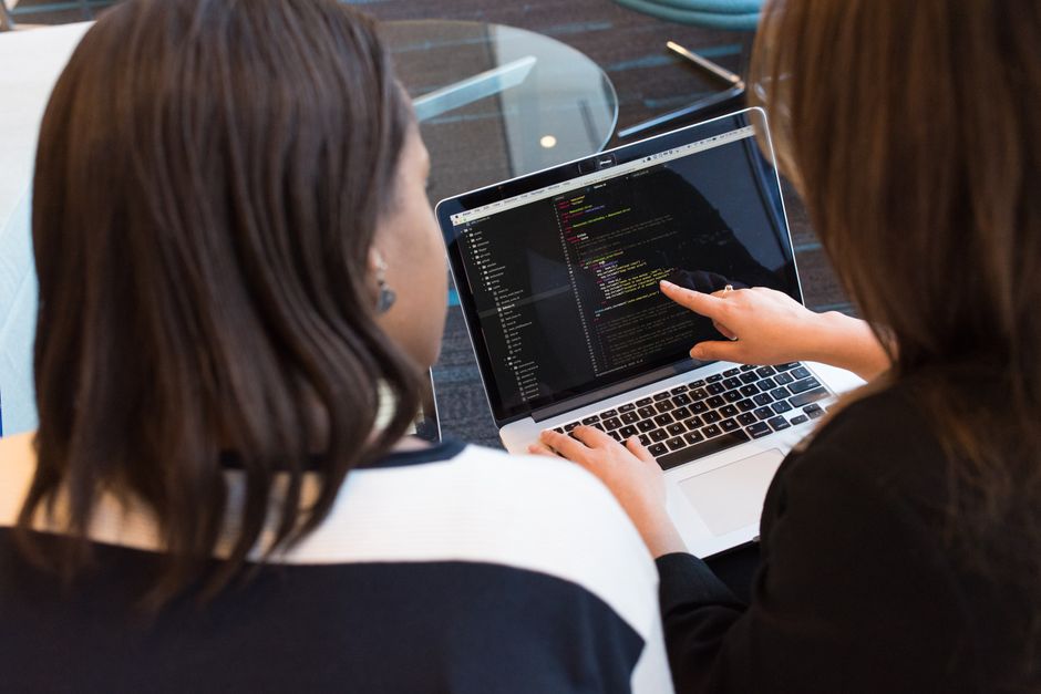 Duas profissionais analisando códigos de programação em um ambiente de trabalho colaborativo.