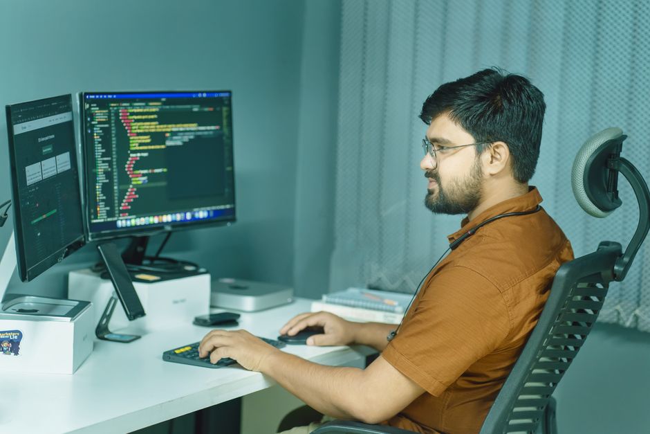 Profissional de tecnologia programando em um ambiente de trabalho com múltiplos monitores exibindo códigos de software, destacando o tema de desenvolvimento de sistemas.