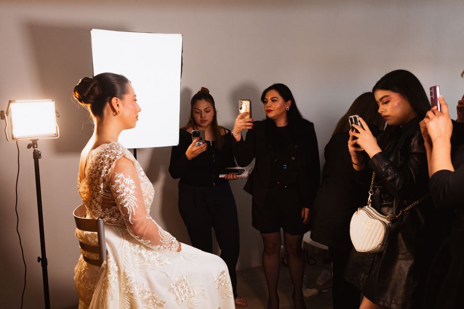 Ensaios fotográficos de moda com uma modelo vestida de vestido de noiva, enquanto profissionais de fotografia ajustam luzes e capturam imagens.