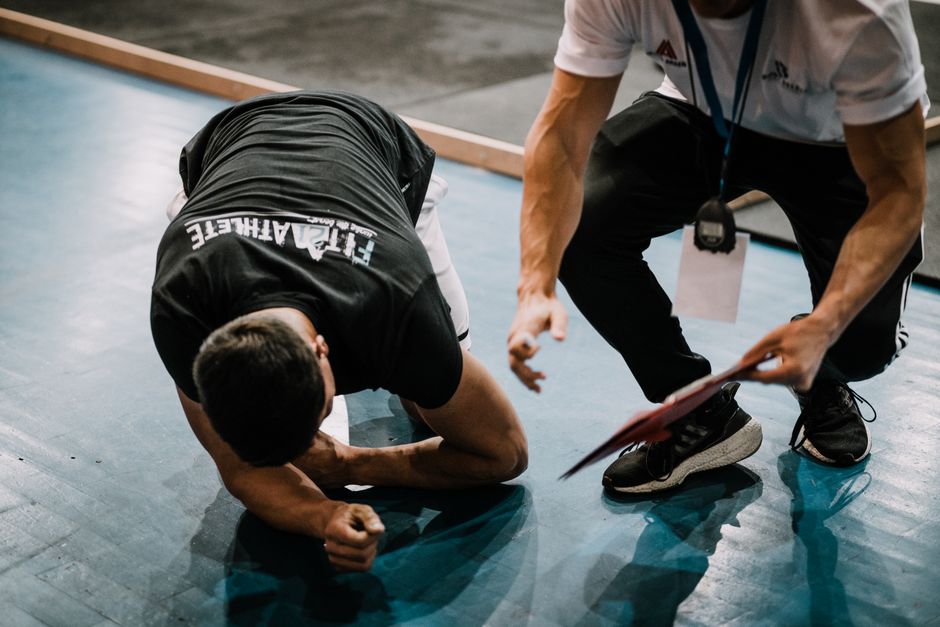 Pessoa se ferindo durante uma atividade esportiva, sendo atendida por um técnico ou staff no local do evento.