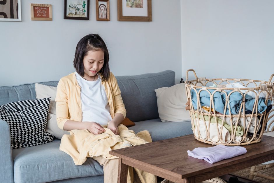 Menina arrumando roupas em casa, ilustrando rotina doméstica e organização do cotidiano.