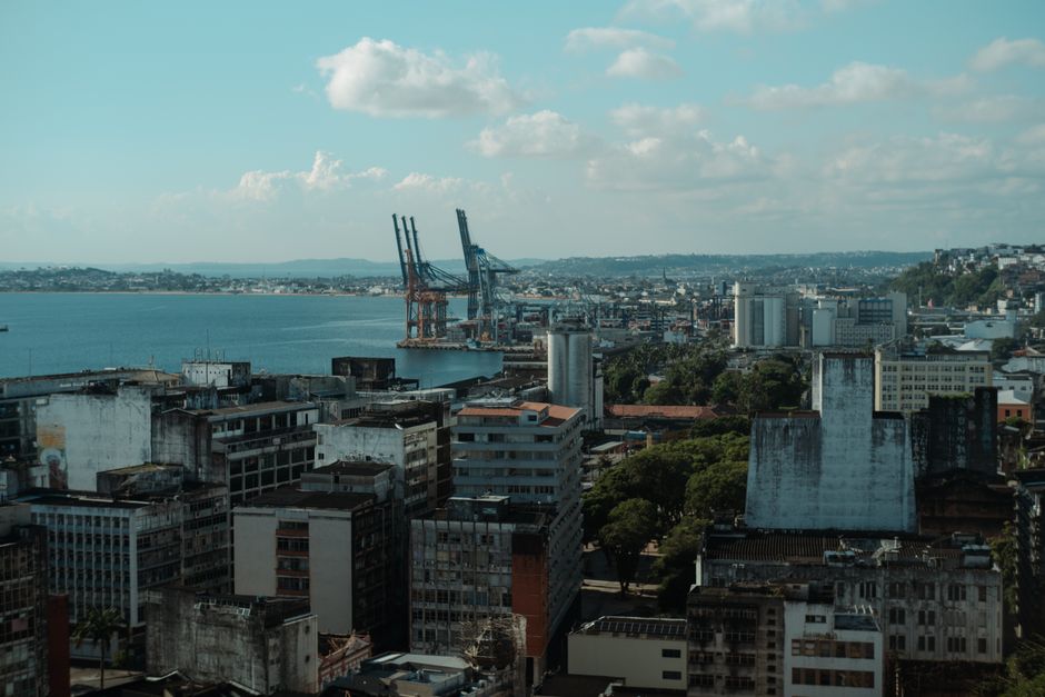 Vista panorâmica de uma cidade portuária com edifícios urbanos e cais industriais sob céu parcialmente nublado.