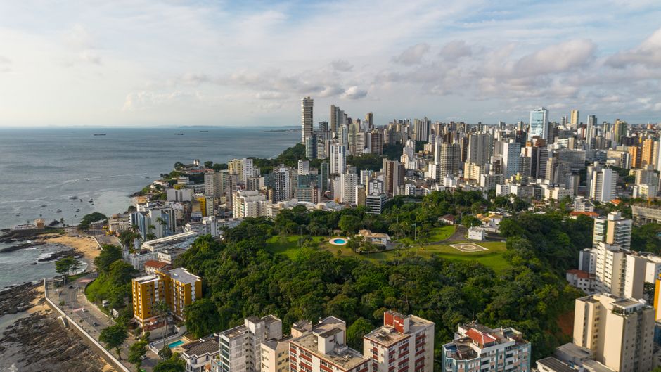 Vista aérea de uma cidade costeira com uma combinação de áreas verdes, prédios altos e litoral, ideal para ilustrar temas urbanos e planejamento urbano sustentável.