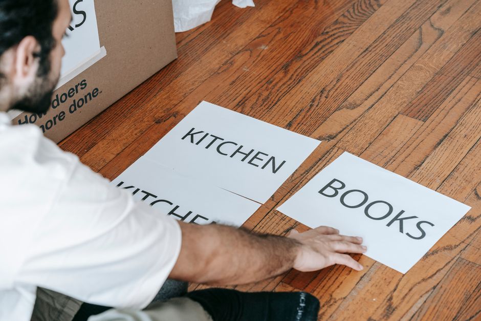 Pessoa organizando categorias de objetos com placas de papel em uma superfície de madeira, representando organização e planejamento doméstico ou empresarial.