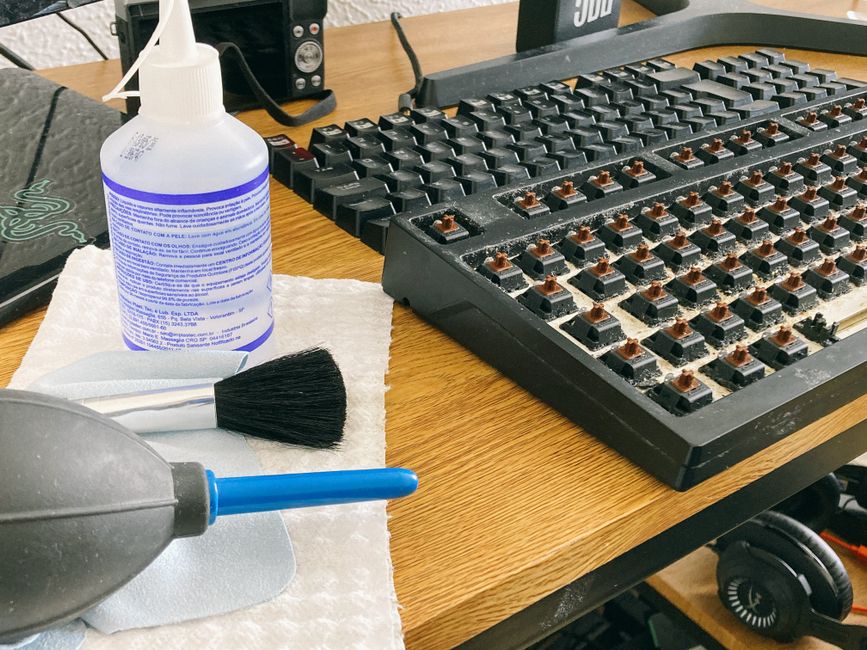 Imagem de uma mesa de workspace sendo limpa, com teclado removido e produtos de limpeza ao lado, sugerindo manutenção de equipamentos de informática.