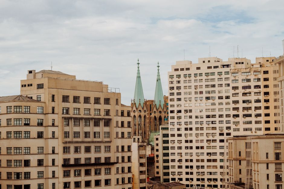 Cena de um cenário urbano com prédios residenciais e uma igreja ao fundo, destacando a convivência entre arquitetura moderna e histórica na cidade.