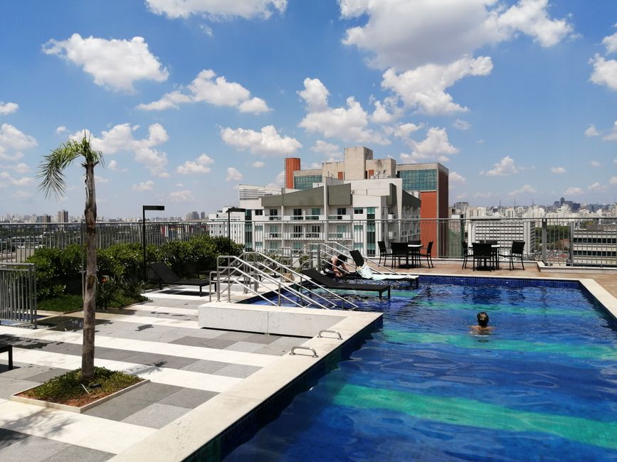 Imagem de uma cobertura de edifício com piscina, área de lazer e vista urbana ao fundo, ideal para artigos sobre lazer em ambientes urbanos e vida de alto padrão.