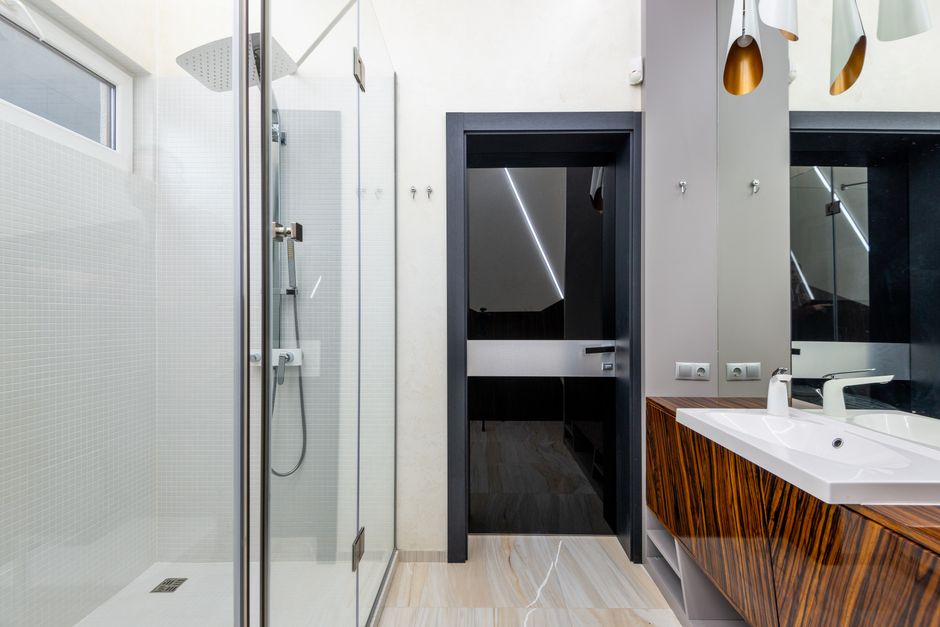Imagem de um banheiro moderno com iluminação de LED, paredes brancas, box de vidro, pia de madeira e detalhes sofisticados, ideal para ilustrar tendências em design de interiores de banheiros.