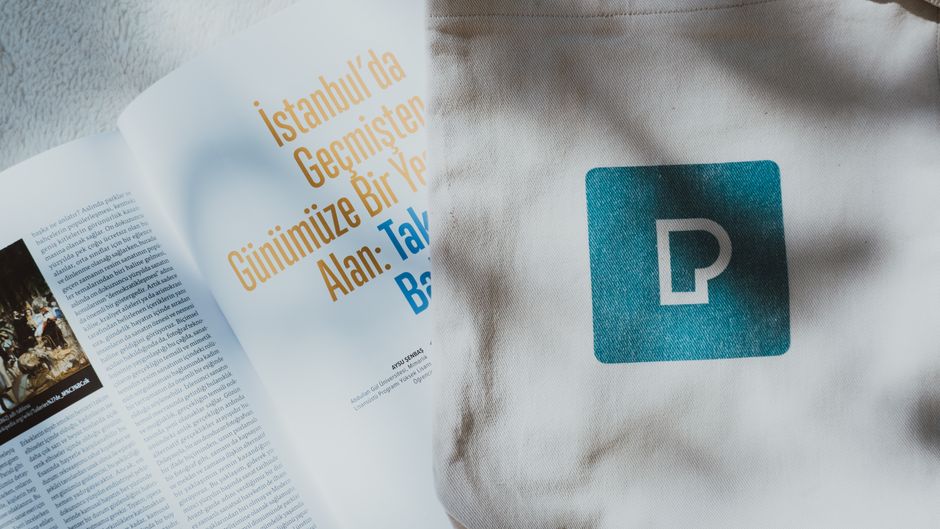 Imagem de uma revista aberta ao lado de uma bolsa de tecido com símbolo de estacionamento, representando planejamento urbano e mobilidade urbana na cidade de Istambul.