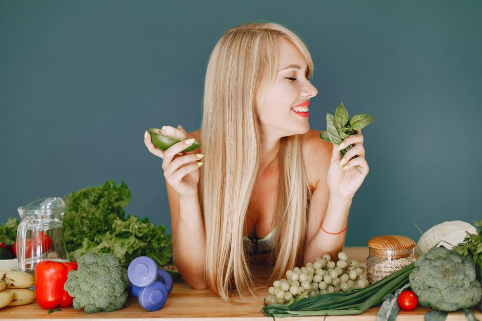 Mulher sorridente desfrutando de uma alimentação saudável com verduras e frutas, simbolizando bem-estar e saúde.