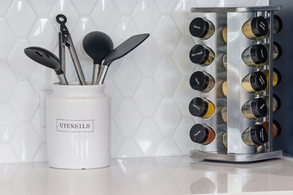 Imagem de uma bancada de cozinha com recipiente de utensílios e especiarias organizadas, trazendo uma estética moderna e funcionalidade.