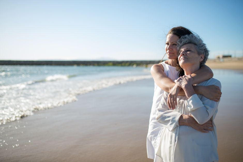 Duas mulheres se abraçando na praia, transmitindo afeto, cuidado e conexão emocional ao ar livre.