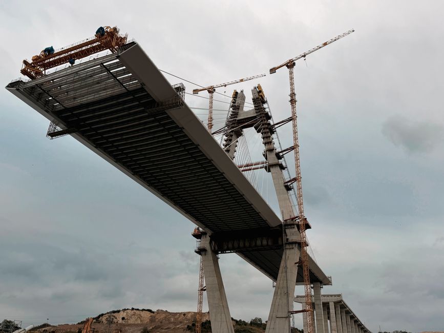 Imagem de uma ponte em construção, com torres de sustentação e guindastes, simbolizando infraestrutura e engenharia.