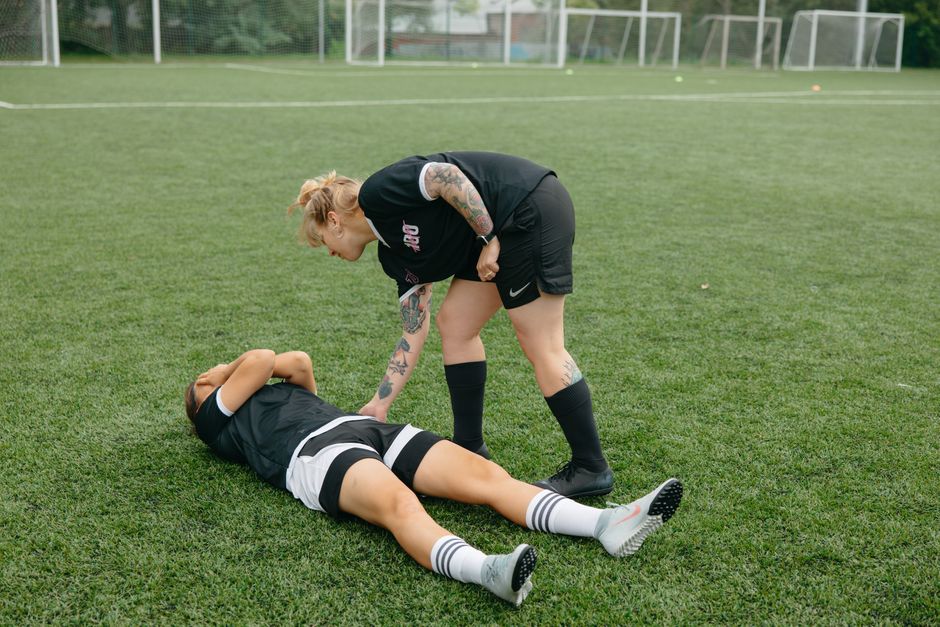 Pessoa inconsciente deitada no campo de futebol enquanto outra pessoa presta primeiros socorros.