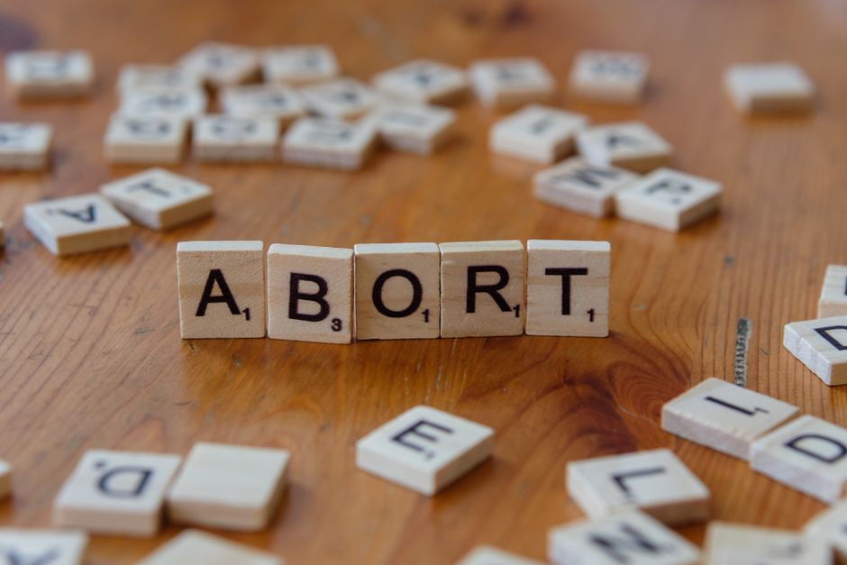 Imagem que simboliza o tema do aborto, com peças de dominó formando a palavra 'ABORT' sobre uma superfície de madeira, ilustrando discussões sociais e éticas.