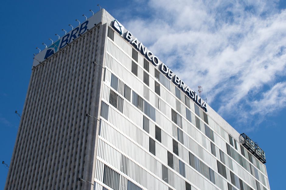 Imagem do edifício do Banco de Brasília (BRB) sob um céu azul com nuvens, simbolizando instituições financeiras e economia.