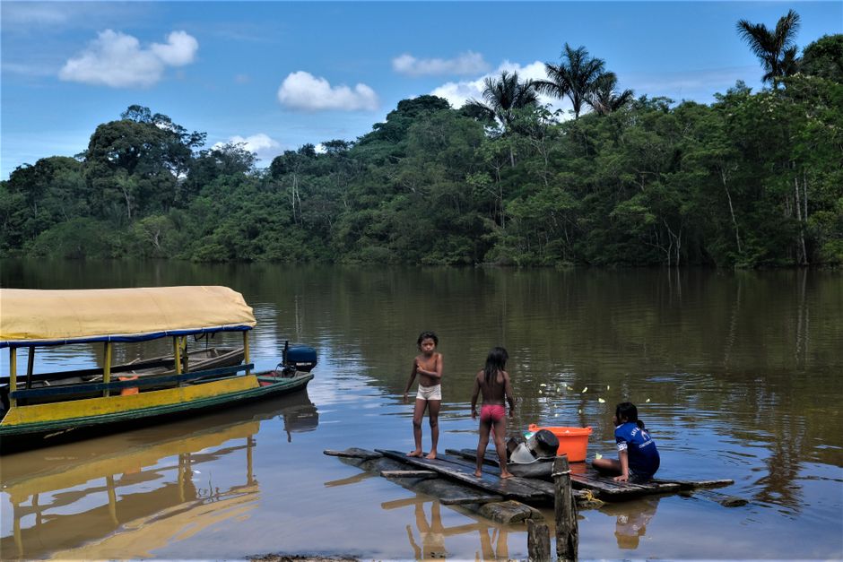 Crianças brincando e se aventurando às margens de um rio na floresta, em um ambiente natural e rústico, típico de comunidades ribeirinhas.