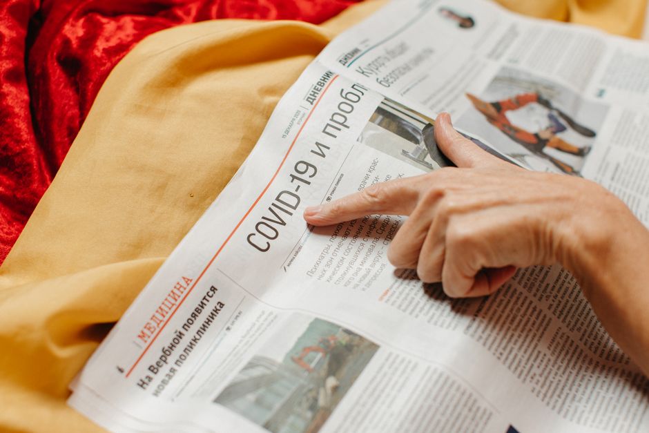 Pessoa lendo um jornal com destaque para notícias sobre a COVID-19, abordando o tema saúde e pandemia.