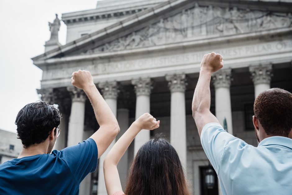 Grupo de pessoas protestando em frente a um edifício clássico, simbolizando luta por justiça social ou direitos civis.