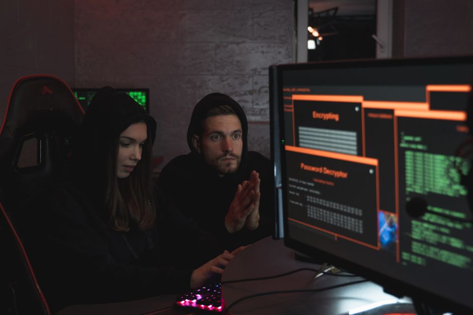 Duas pessoas analisando códigos de programação e atividades de hacking em um ambiente de tecnologia e segurança digital.