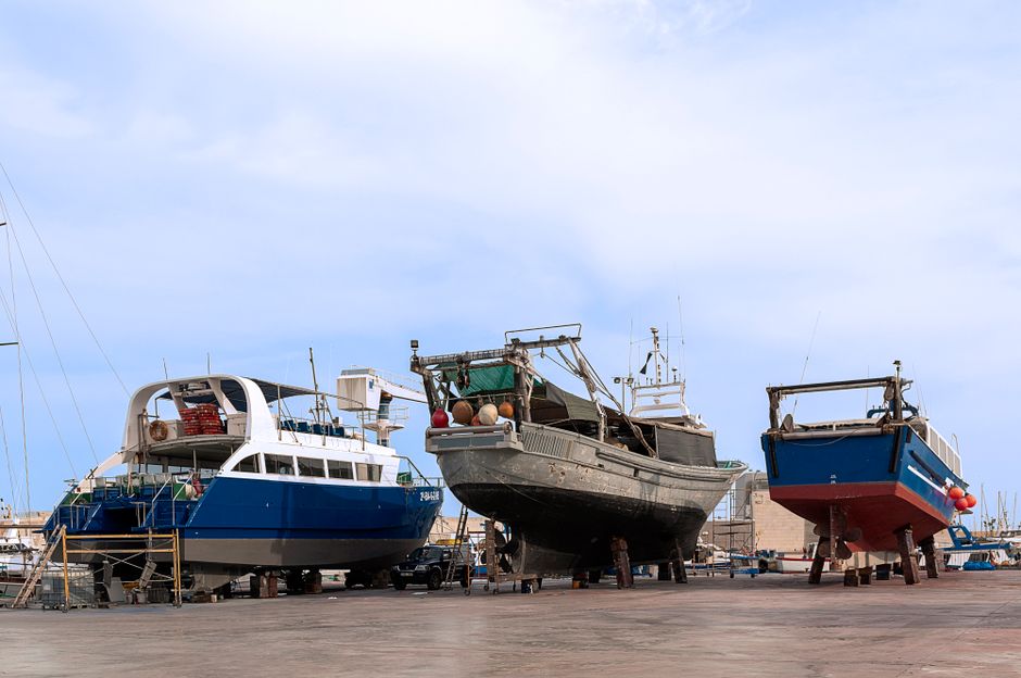 Imagem de barcos de pesca e embarcações de diferentes tamanhos em um estaleiro, representando atividades marítimas e comércio naval.