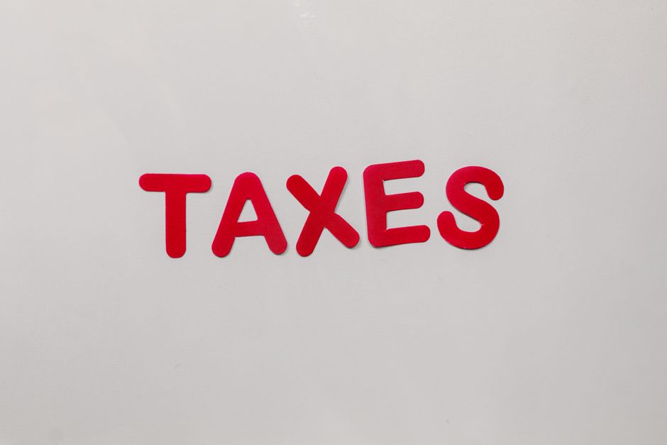 Imagem de letras em destaque com a palavra 'TAXES' em um fundo branco, abordando o tema de obrigações fiscais e tributárias.
