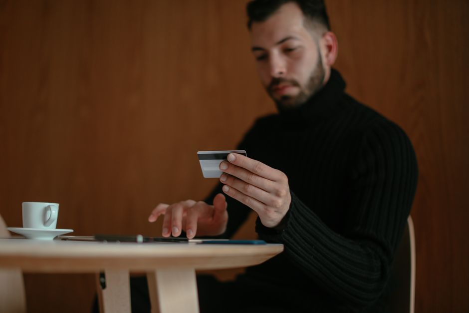 Homem realizando uma transação financeira utilizando um cartão de crédito em ambiente interno com fundo de madeira.