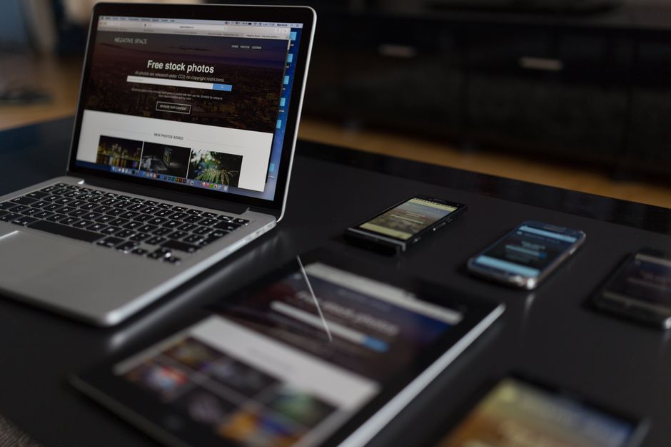 Imagem de mesa de trabalho com laptop, smartphones e tablet, representando atividades digitais e comunicação online.