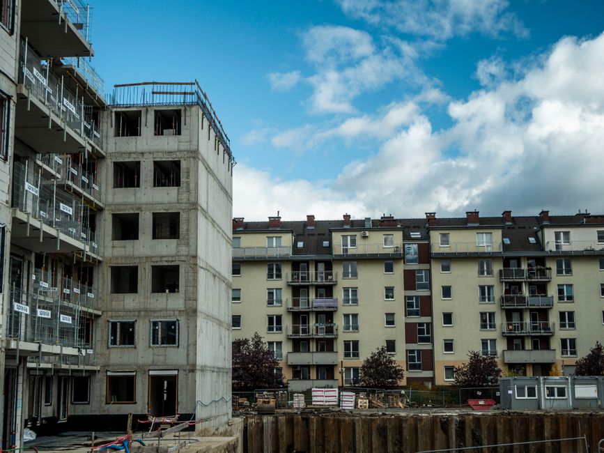 Imagem de um prédio em construção ao lado de uma edificação residencial já concluída, representando o desenvolvimento imobiliário e obras civis.
