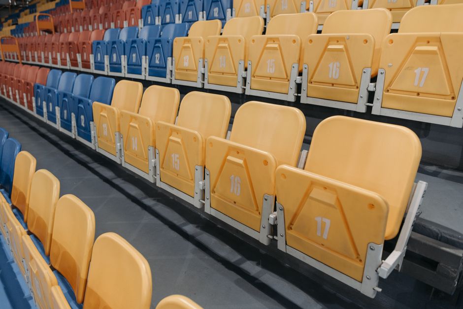 Imagem de arquibancadas de ginásio ou estádio com assentos coloridos organizados em filas.