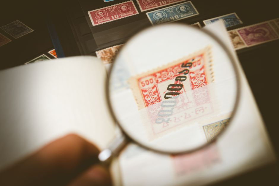 Imagem de uma coleção de selos históricos, visualizada através de uma lupa, destacando o tema de colecionismo ou história postal.