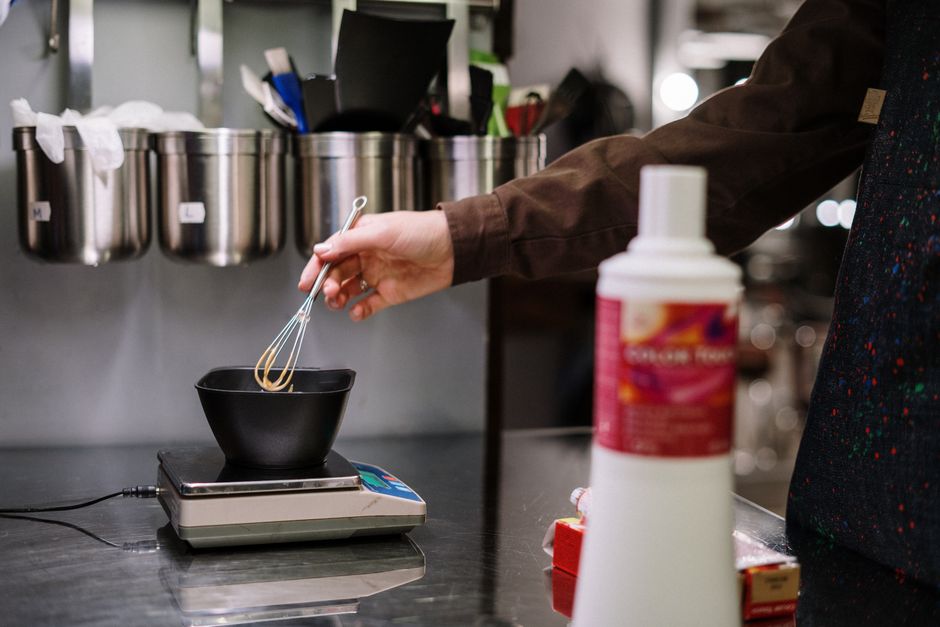Pessoa preparando uma mistura usando um batedor em uma batedeira de precisão em um ambiente de cozinha industrial.