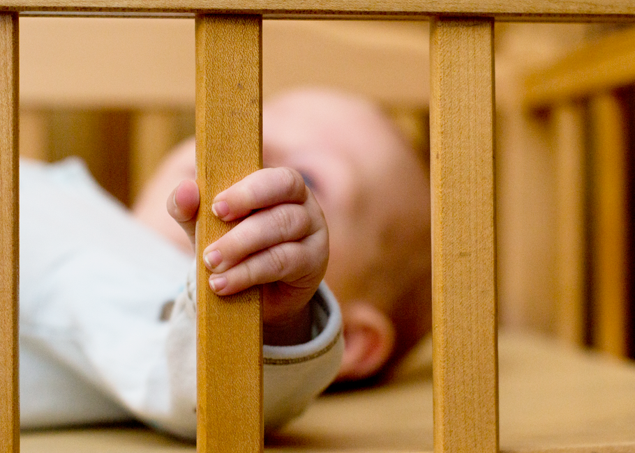 Bebê brincando de esconde-esconde atrás de uma grade de cama, transmitindo uma sensação de inocência e exploração infantil.