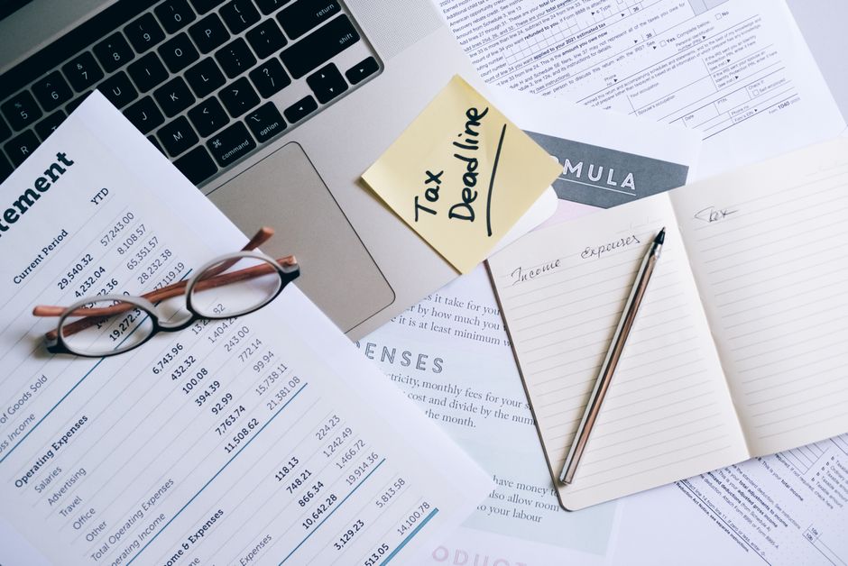 Imagem de uma mesa de trabalho com documentos financeiros, uma nota sobre imposto de renda pendurada e uma xícara com óculos, relacionada ao tema de planejamento fiscal e gestão financeira.