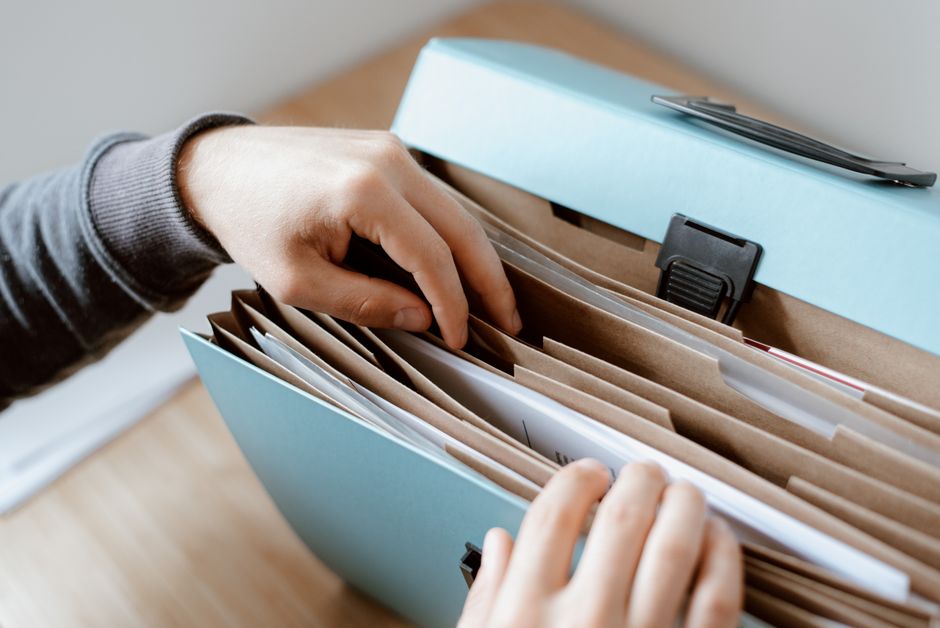 Pessoa organizando documentos em uma pasta de arquivo, representando gestão de informações ou rotina administrativa.