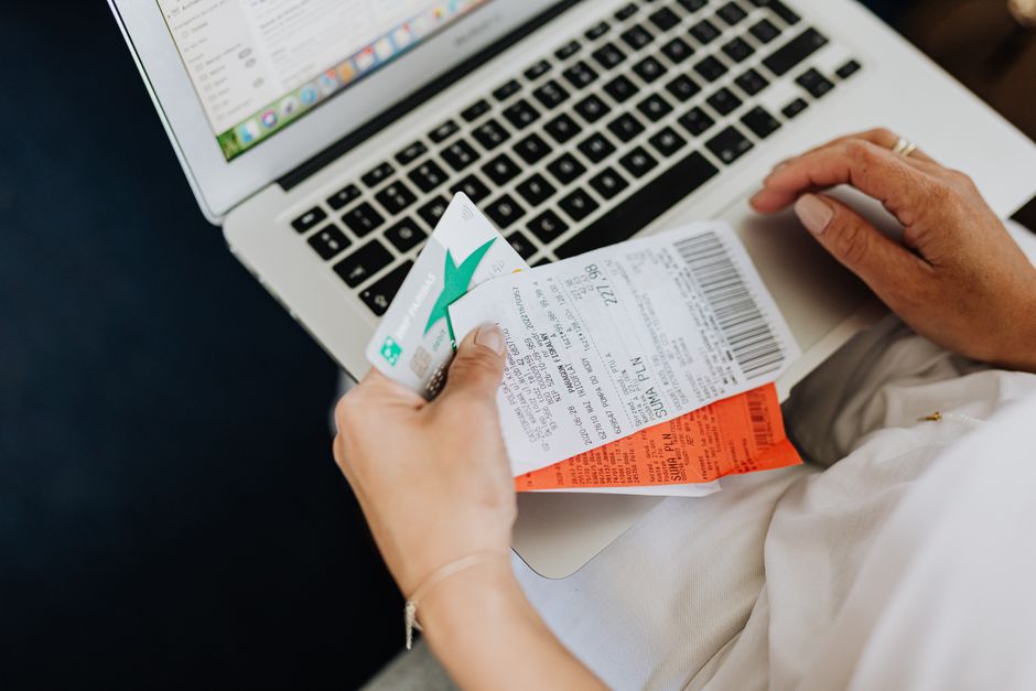 Pessoa organizando faturas de viagens enquanto trabalha no notebook, simbolizando planejamento financeiro para viagens ou controle de despesas.