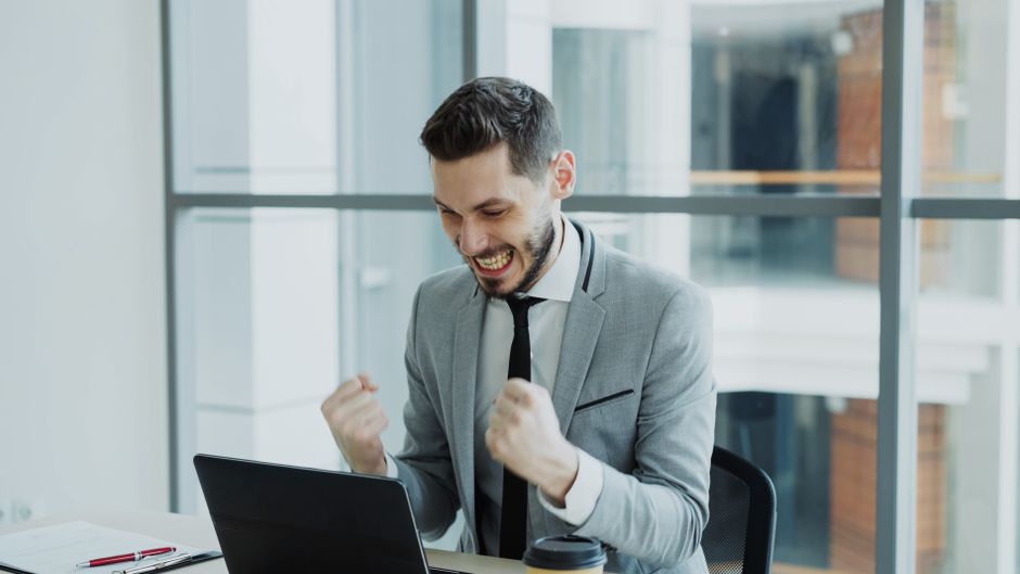 Homem celebrando uma conquista ou sucesso profissional em ambiente de escritório, transmitindo entusiasmo e realização.