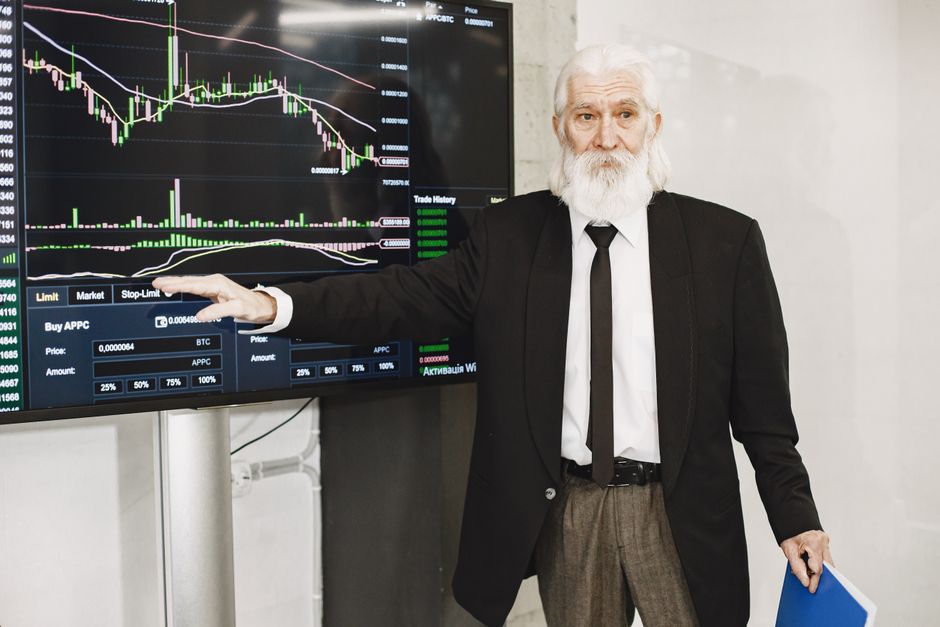Homem idoso apresentando análise de gráficos de mercado financeiro em uma sala de reunião moderna.