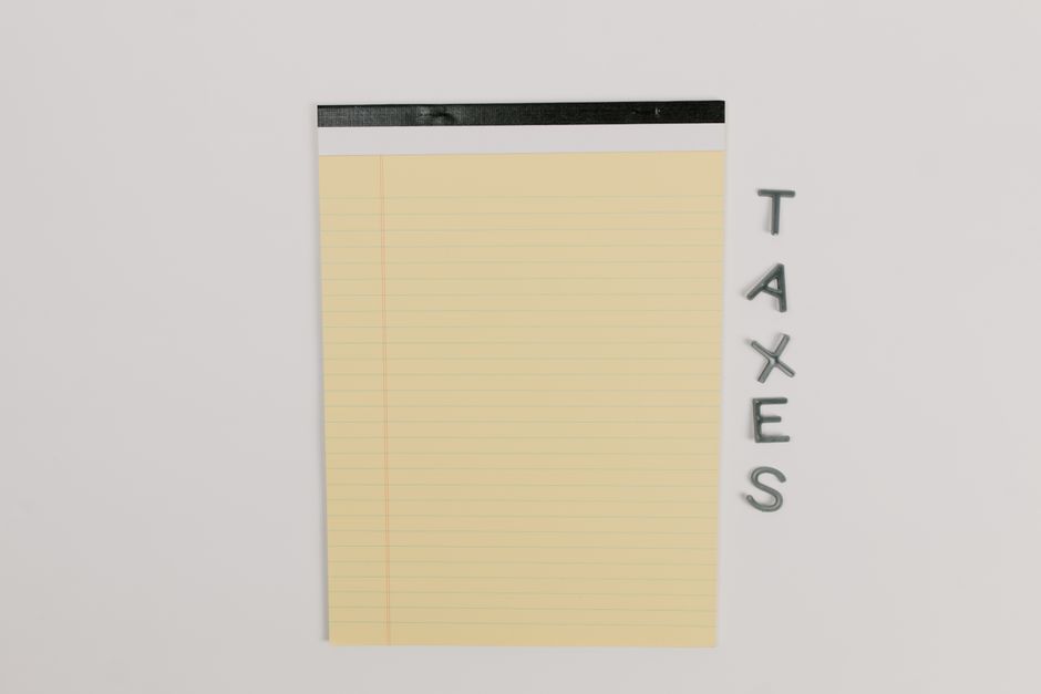 Folha amarelo com linhas para anotações ao lado de letras formando a palavra 'TAXES', representando organização e planejamento tributário para blog de assuntos fiscais.