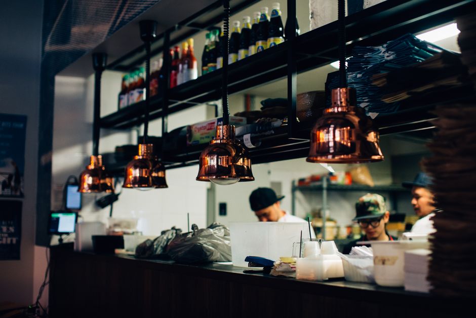 Cena de uma cozinha de restaurante com funcionários trabalhando, destacando o ambiente de preparação de alimentos e equipe de cozinha em ação.